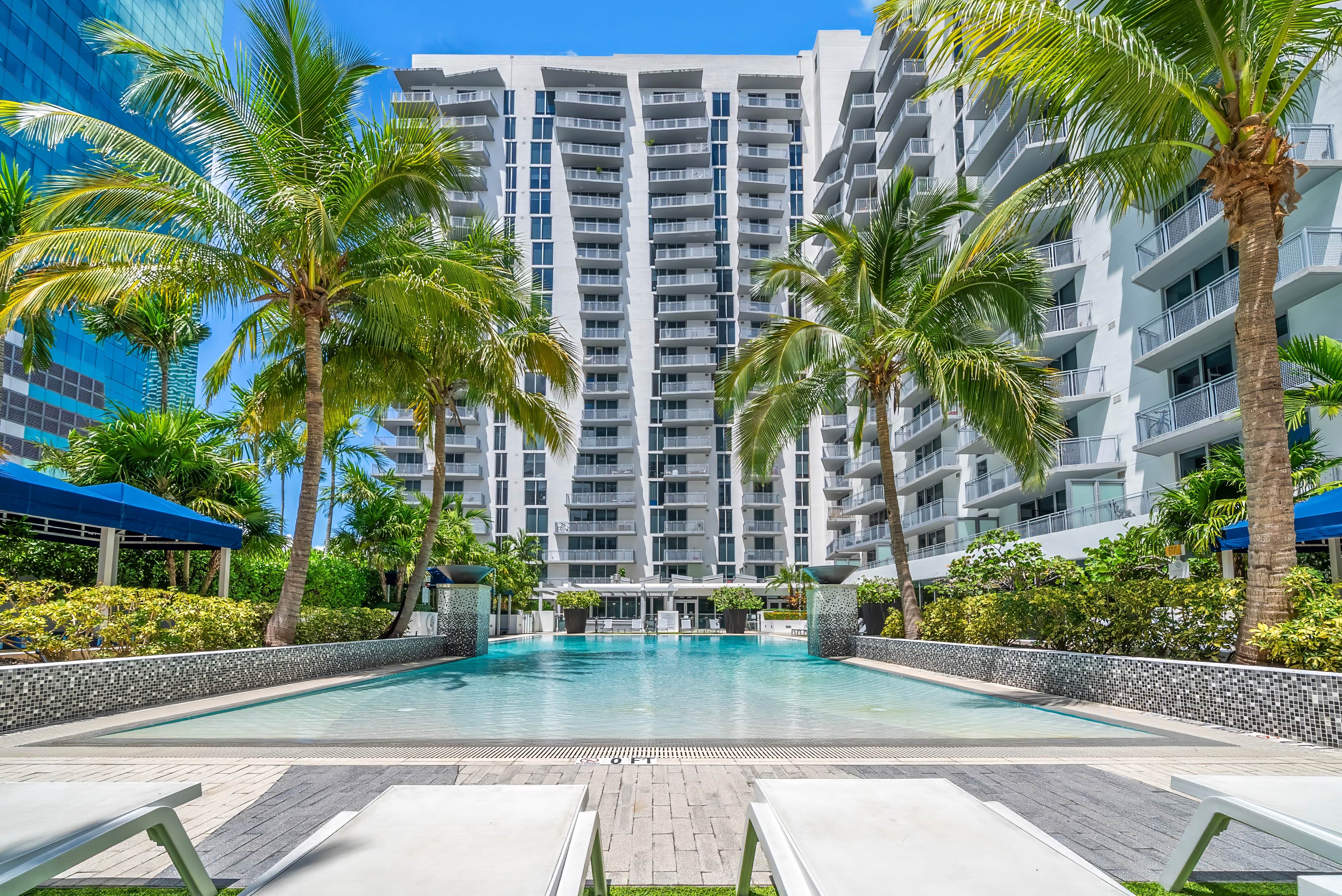 Lounge, Swim, Repeat resort style pool with palm trees and a building behind