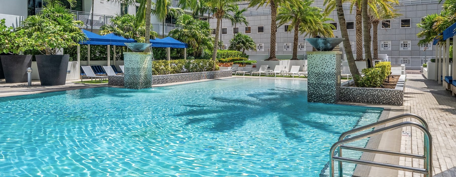 resort style pool with seating palm trees and a building behind it